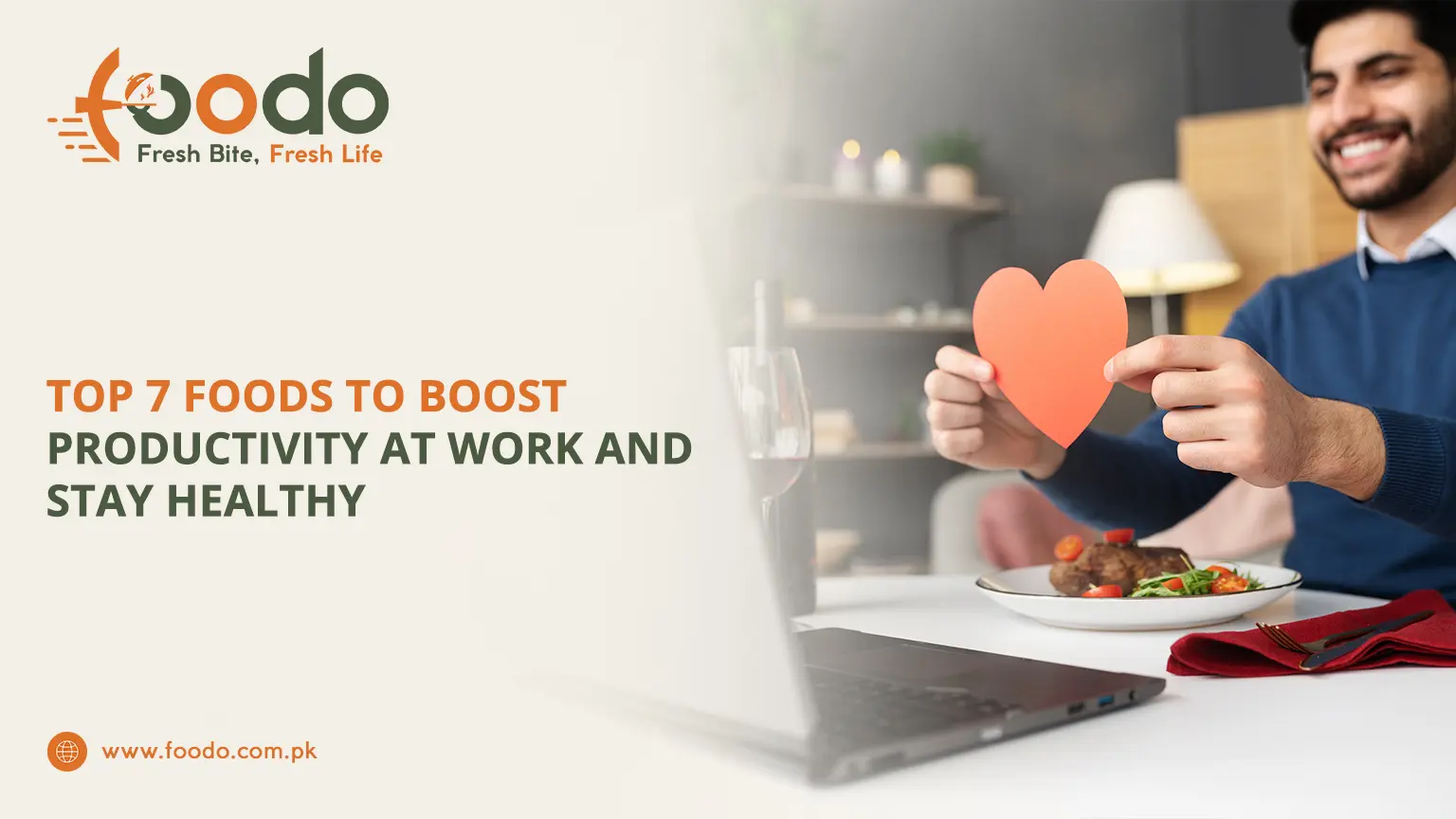 Smiling young professional at work holding red heart shape, sitting at desk with laptop and healthy balanced meal plate, boosting productivity and staying healthy